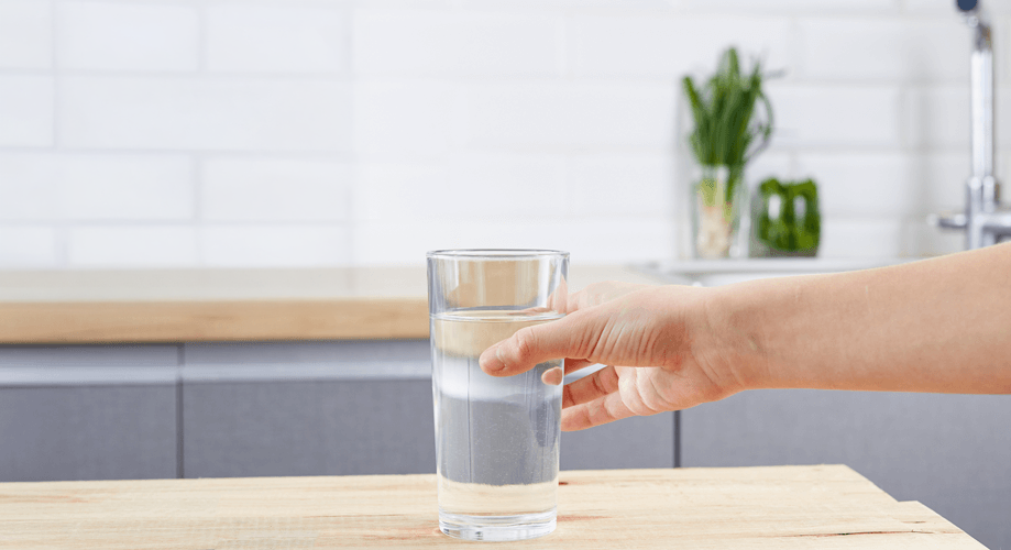 Verre d’eau pure tenu par une main dans une cuisine blanche au style épuré